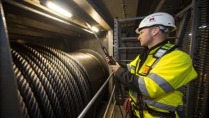 Elevator technician inspecting steel wire ropes in an elevator shaft